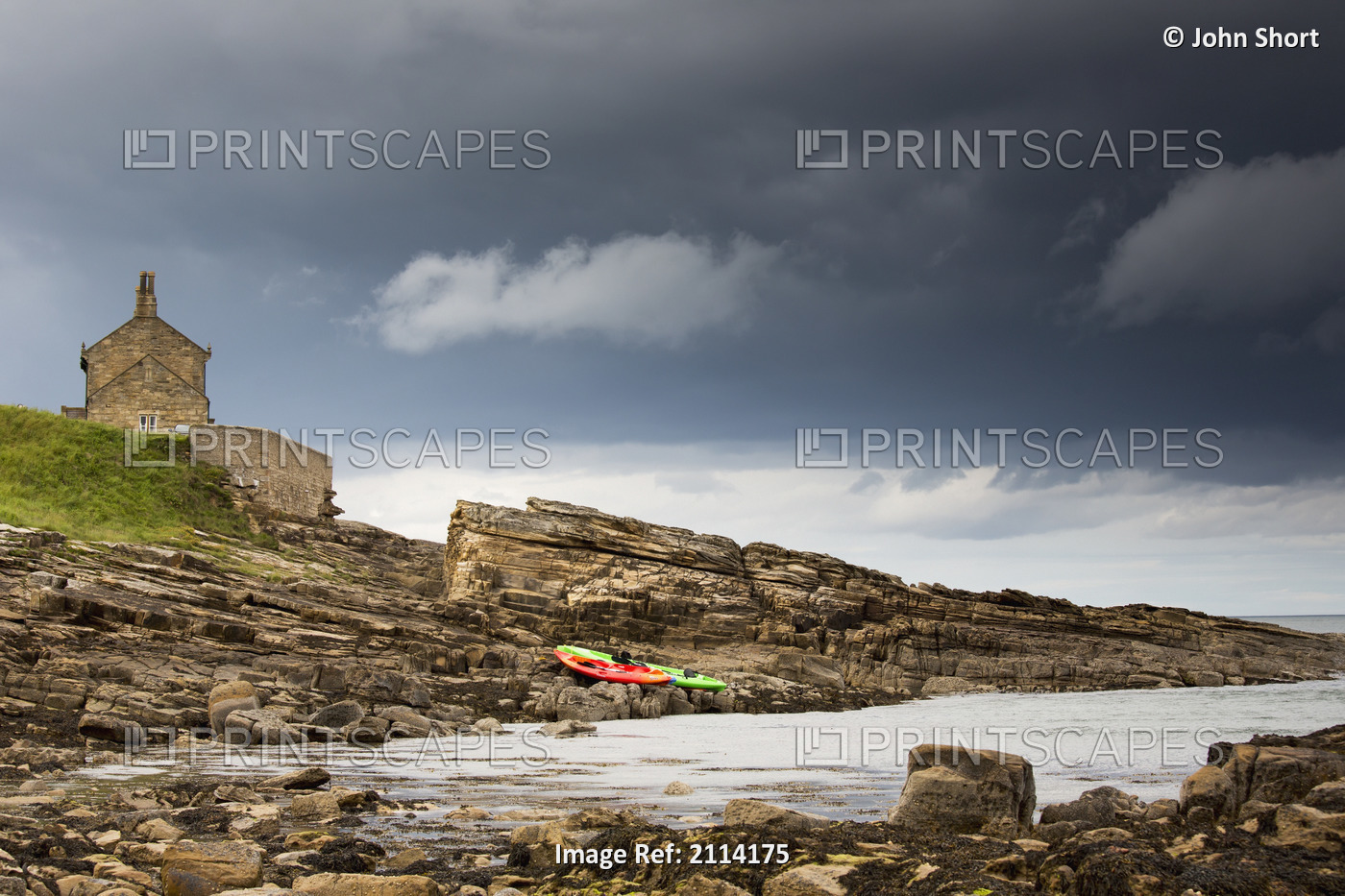 Red And Green Kayaks Sitting On The Rocky Shore With A House At The Water's ...