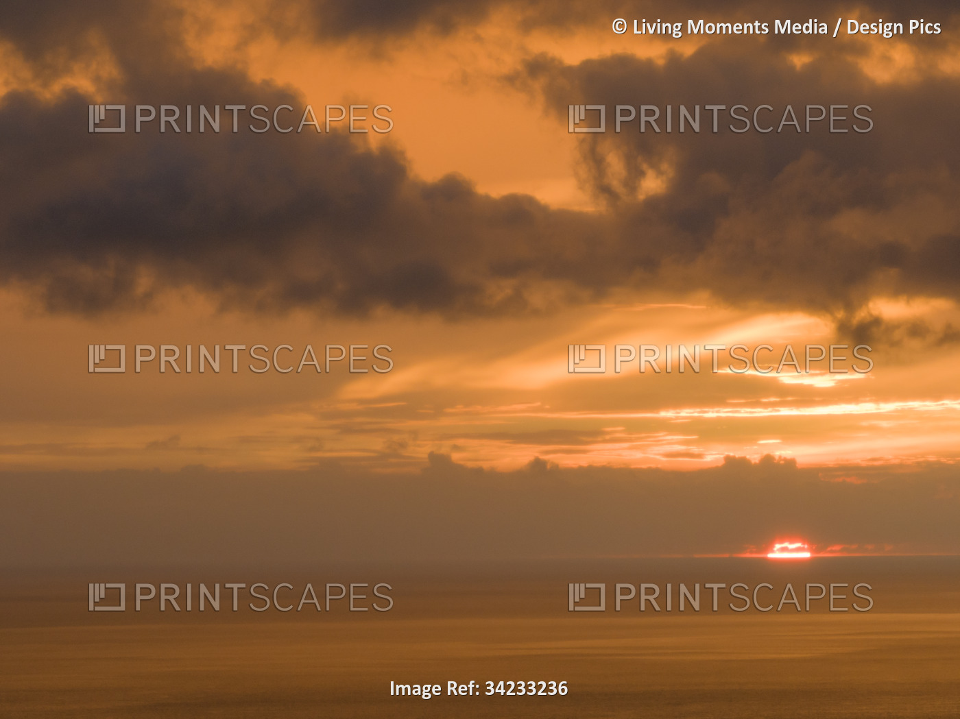 Dramatic sunset through clouds and over the ocean's horizon, showing a warm ...